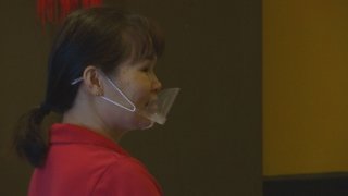 Woman with a red shirt wearing a clear plastic mask over her mouth.