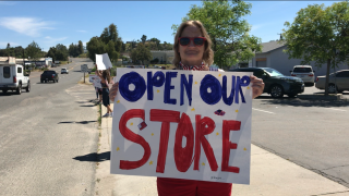Woman holds "open our store' sign at rally in Ramona