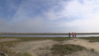 Three people stand along the shore of a river estuary