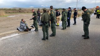 agentes del patrulla fronteriza frente a inmigrante sentado en el suelo con una cobija