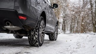 Close-up of winter car tires in a winter scenario with snow and trees in a mountain road