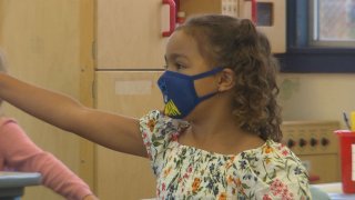 Girl wearing a mask raises her arm in a classroom