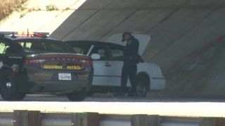 CHP officer inspecting white sedan involved in freeway shooting.