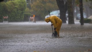 A worker attempts to clear a drain in a flooded street.