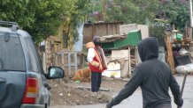 Hombre frente a una casa de pedazos de madera y una lona de plástico como techo