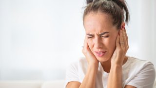 Woman closes hear ears with hands due to noise. FILE