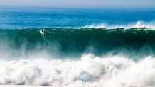 A surfer paddles over a giant wave at Blacks Beach in San Diego, California