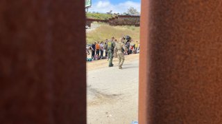 From between the U.S.-Mexico border, a U.S. border patrol agent oversees migrants near San Ysidro on Thursday, May 11, 2023.