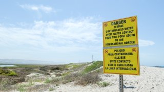 Un cartel bilingüe junto al río Tijuana y el océano Pacífico advierte a la gente que evite el contacto con aguas contaminadas por aguas residuales.