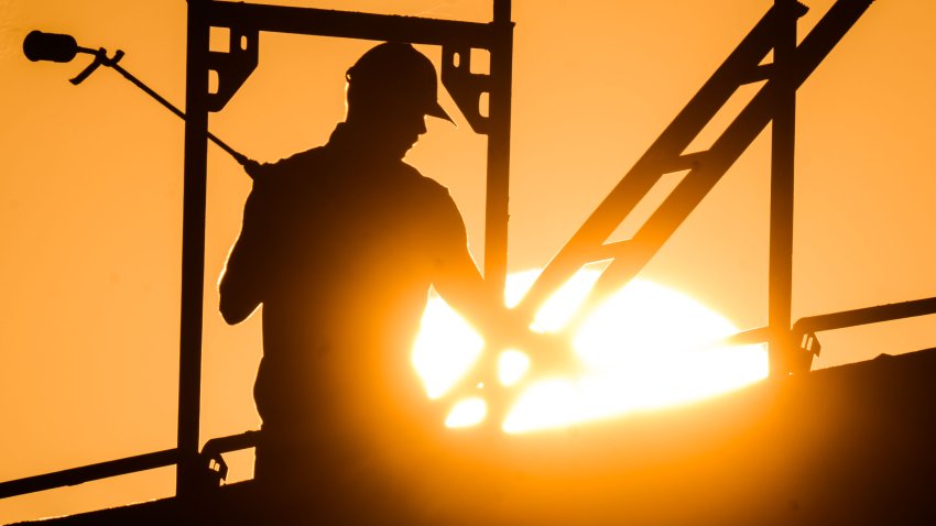 12 August 2022, Lower Saxony, Hanover: A construction worker stands with a gas burner during the construction of an apartment building in the Kronsrode development area as the sun rises on the horizon. The persistent heat is an enormous burden for many workers. Photo: Julian Stratenschulte/dpa (Photo by Julian Stratenschulte/picture alliance via Getty Images)