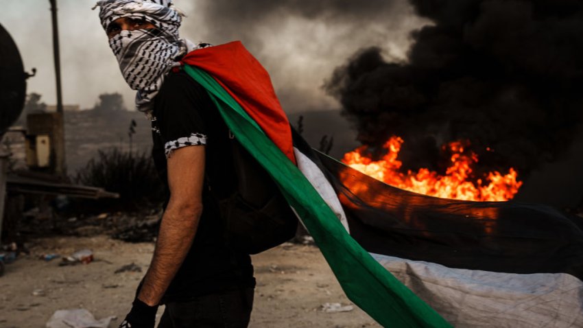 RAMALLAH, ISRAEL — OCTOBER 13, 2023: A Palestinian dons a Palestinian flag during while protesting Israeli occupation in the West Bank, as protesters are met with tear gas, flashbang and live fire from Israeli forces, in Beit El area of Ramallah, Israel, Friday, Oct. 13, 2023. Tensions are rising all across Israel and Palestinian Territories as IsraelÕs military prepares for a wide scale incursion into Gaza in the countryÕs south. (MARCUS YAM / LOS ANGELES TIMES)