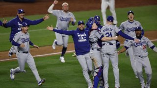 El lanzador de los Dodgers de Los Ángeles, Walker Buehler (3-d), es abrazado por el receptor de los Dodgers, Will Smith (4-d), mientras sus compañeros de equipo celebran después del último out contra los Yankees de Nueva York en el quinto juego para ganar la Liga Mayor de Béisbol.