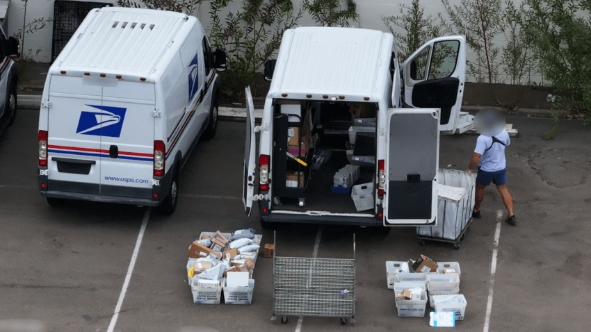 A postal worker loads mail onto a USPS mail.