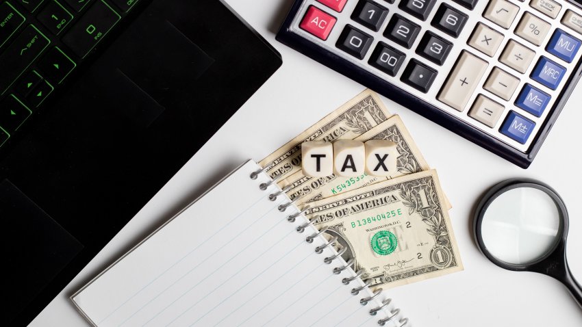 Tax word written on an office table with laptop, calculator, US dollars and diary on it.