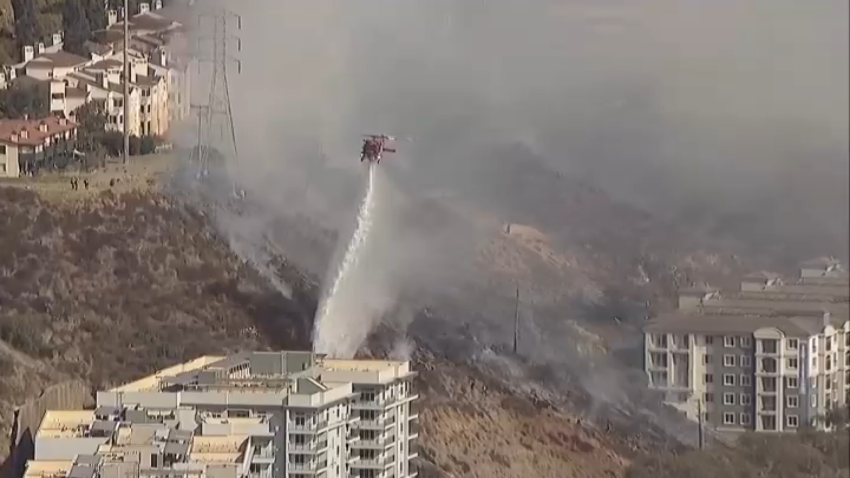 A helicopter drops water above a brush fire in Mission Valley near the Fashion Valley Mall, Jan. 21, 2025.