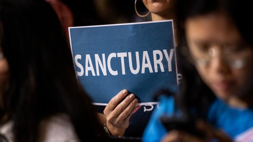 A woman in the audience holds up a poster with a message of support for immigrants as the Los Angeles City Council considers a “sanctuary city” ordinance during a meeting at City Hall in Los Angeles, California, on November 19, 2024. The proposed sanctuary city ordinance would prohibit any city resources from being used  to help federal enforcement of immigration laws. (Photo by ETIENNE LAURENT / AFP) (Photo by ETIENNE LAURENT/AFP via Getty Images)