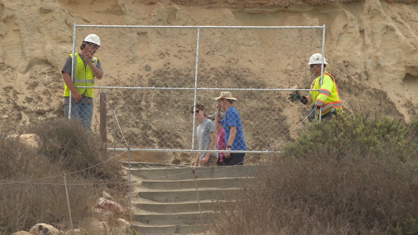Workers place a chainlinked fence on a hillside.